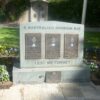 Three small plaques set in a stone in front of lawn area and near flowers