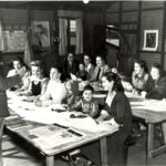 Image: man standing in front of group of women and children sitting at desks