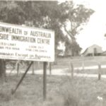 Image: sign amongst gum trees with buildings in background