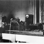 Image: A man sits at a bench full of telegraphic instruments