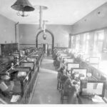 Image: Inside an office. Benches are partitioned into desks and occupied by a number of men.