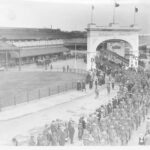 Image: Large group of men in uniform walking through arch and along path