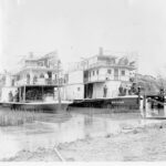 Image: Black and white photograph of two paddlesteamers anchored next to each other on a river. The paddlesteamer on the left is flying the Union Jack