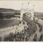 Image: Large group of men in uniform walking through arch and along path