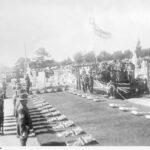 Image: Men in uniform stand to attention several people standing between flags