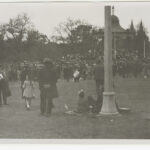 Image: a large group of men, women and children gather around a rotunda in a park