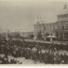 Image: A large group of people in 1880s dress stand in distinct lines in front of a large building with a domed roof which is decorated with flags and bunting.