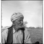 Image: An elderly man with a beard and turban stands in the central Australian desert