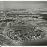 Image: An aerial view of several large buildings arrayed in rows in a largely flat, agricultural landscape