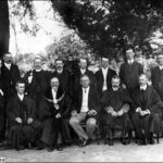 Image: A group of men in Edwardian attire pose for a photograph. One of the men is wearing a large mayoral collar