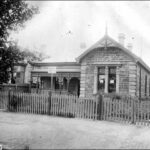 Image: A large stone cottage with iron lacework surrounding its front verandah