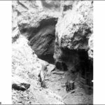 Image: A man stands at the bottom of a large crevasse. Next to the man is a wheeled bin, as well as partial timber structure