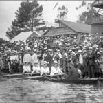 Image: A large crowd watches four female rowers and their male cox