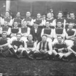 Image: A uniformed sports team poses for a photograph. A man in suit and hat sits in the centre of the group