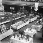 Image: A man examines flowers at a table in a large open hall