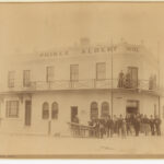 Image: A group of men standing in front of the Prince Albert Hotel. Three women are standing on the balcony.