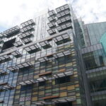 Image: A modern multi-storey building with multiple coloured wall panels and an oval conical tower at one corner