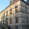 Image: A large, two-storey historic stone building with red doors and a sign reading South Australian Museum