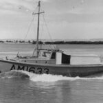 Image: A small motor boat travels along a river. The riverbank and distance hills are visible in the background