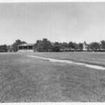 Image: A large, open sports oval containing a cricket pitch and soccer goal. The oval’s grandstand is visible in the background