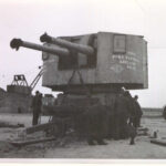 Image: A small group of men work near the base of a large battleship turret with two cannons