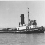 Image: A tugboat with ‘Yelta’ painted on its bow underway in a river. A distant riverbank is visible in the background