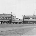 Image: A small, single-storey shop is sandwiched between two large multi-storey buildings. A sign above the shop’s front door reads: ‘Wm. Russell’