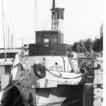 Image: A derelict tugboat is moored against a wharf. Another boat is moored against the starboard side of the tug