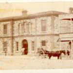 Image: A horse-drawn cart parked in front of three bluestone buildings.