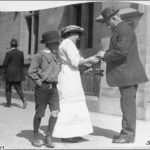 Image: A woman is selling some wattle plant to a man in the street as a young boy looks on, a man walks by in the background