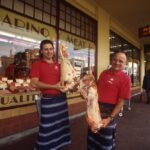 Image: two men holding meat in front of butchers shop