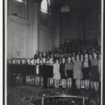 Image: A large choir of children singing with a piano in the foreground.