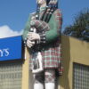 Image: large painted figure of a man in a kilt playing the bagpipes