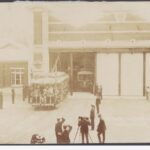 Image: Photograph of the State Herbarium in 1909 showing a decorated tram coming out of the 'tram barn', with men saluting either side of the procession and photographers taking pictures