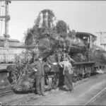 Image: Front view of a train decorated in foliage, two men stand at the front of the train